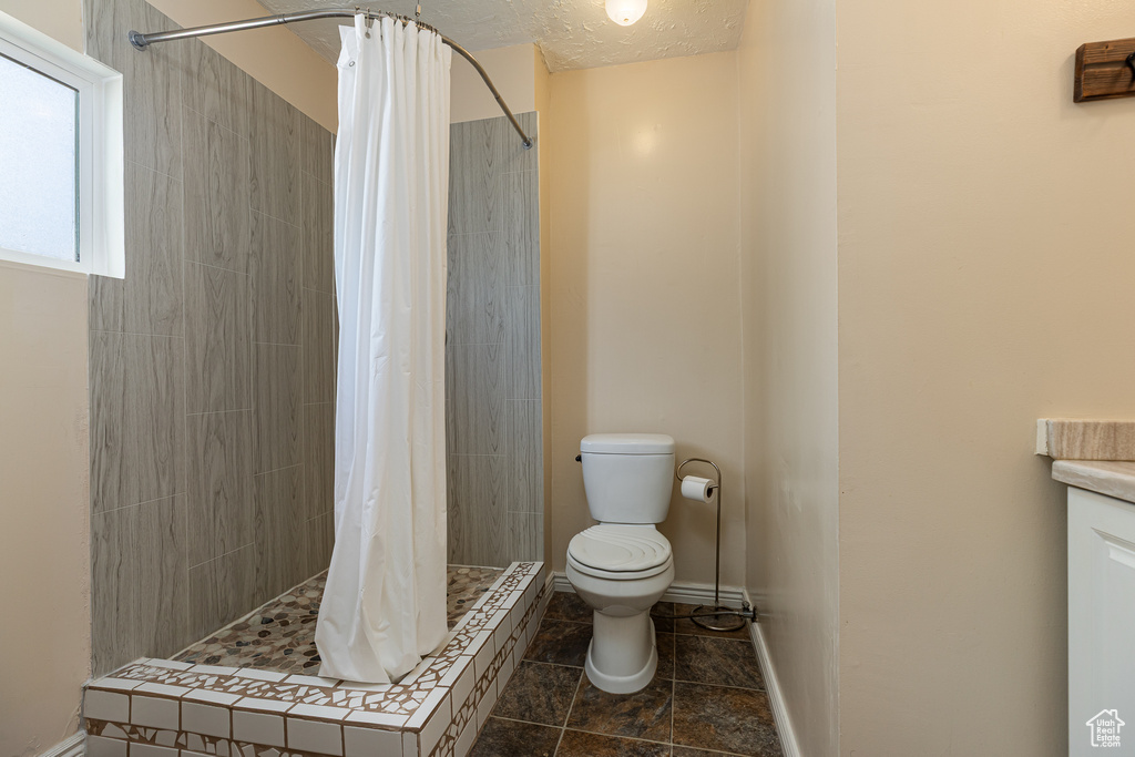 Bathroom with tile patterned flooring, toilet, baseboards, a textured ceiling, and a stall shower