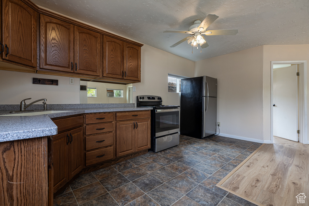 Kitchen with ceiling fan, appliances with stainless steel finishes, a sink, baseboards, and stone finish flooring