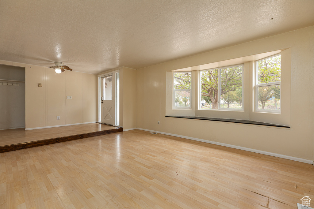 Unfurnished room with light wood-style floors, baseboards, a ceiling fan, and a textured ceiling