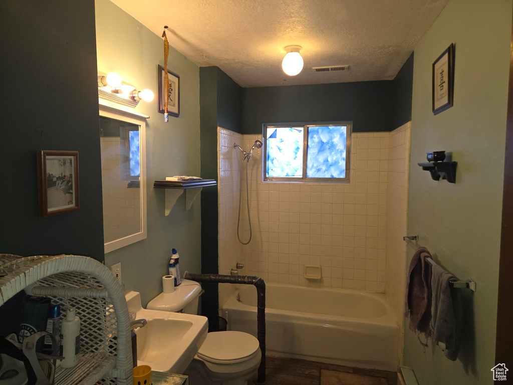 Full bathroom with visible vents, wood finished floors, toilet, bathtub / shower combination, and a textured ceiling