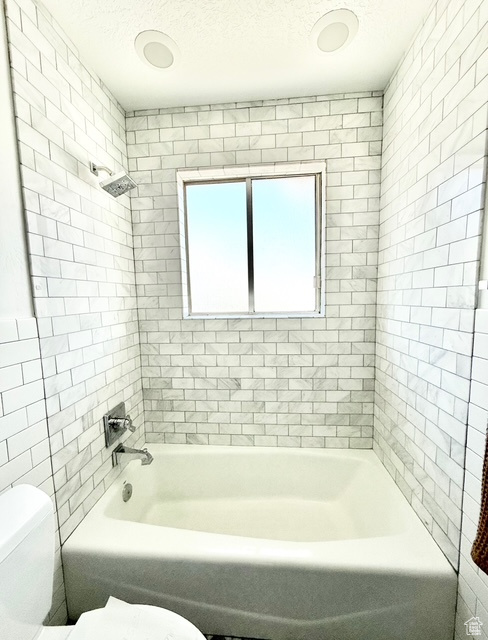 Bathroom with  shower combination, a textured ceiling, toilet, and tile walls