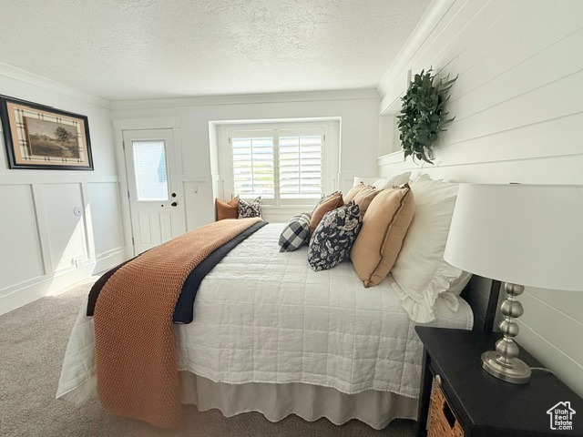 Carpeted bedroom with crown molding, a decorative wall, and a textured ceiling