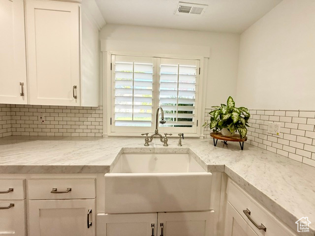 Kitchen with visible vents, light stone countertops, white cabinets, tasteful backsplash, and a sink