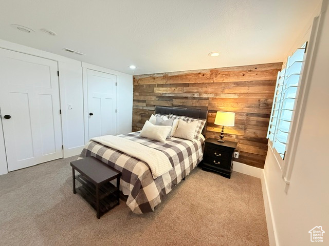 Bedroom featuring wooden walls, visible vents, multiple windows, and light colored carpet
