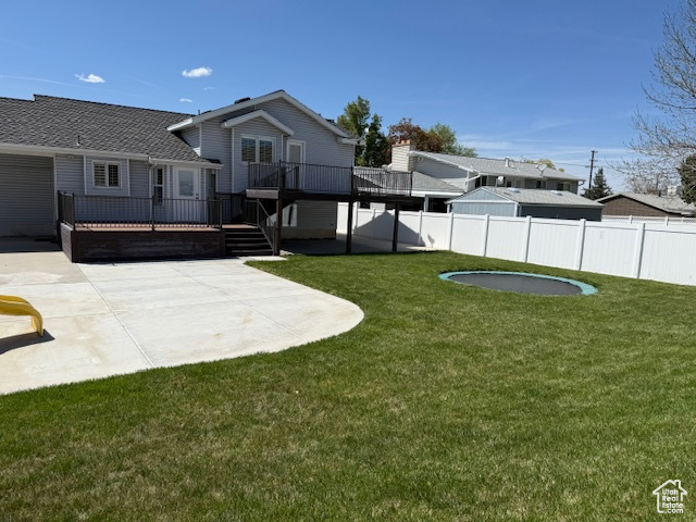 View of yard with a patio, an attached garage, a wooden deck, and fence