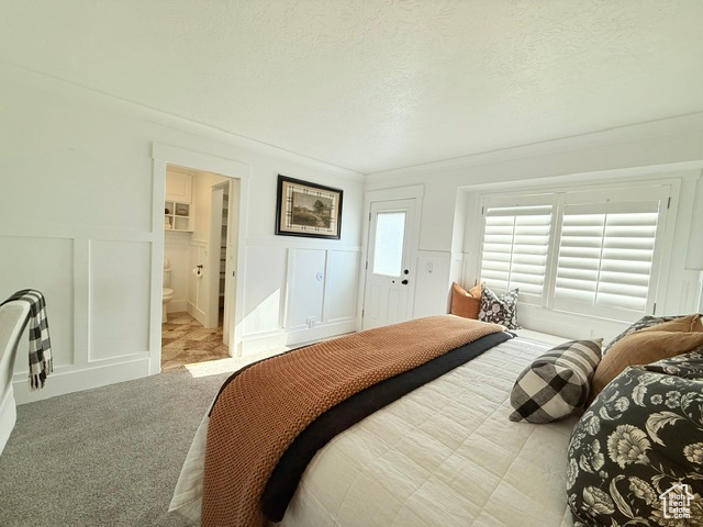 Carpeted bedroom with a textured ceiling, a wainscoted wall, ensuite bathroom, and a decorative wall