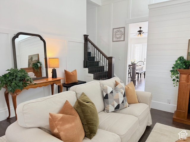 Living room with dark wood-style flooring, a ceiling fan, stairway, and a decorative wall