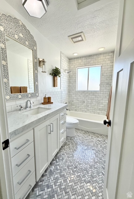 Bathroom with vanity, a textured ceiling, tub / shower combination, and toilet