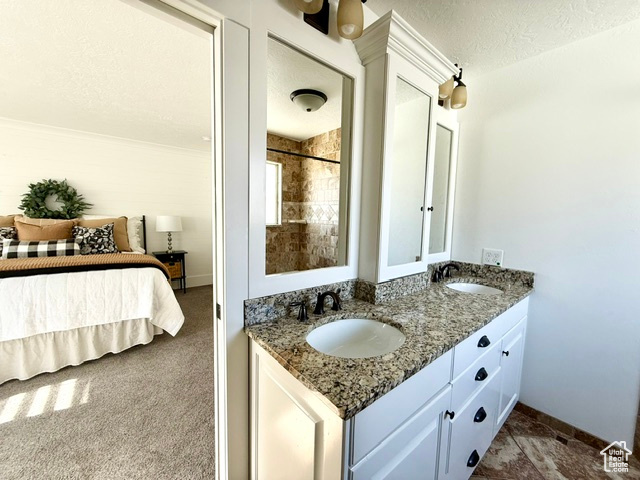 Full bath featuring double vanity, a sink, a textured ceiling, and baseboards