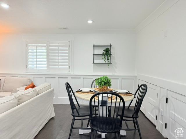 Dining area with recessed lighting, a wainscoted wall, a decorative wall, dark wood-style floors, and crown molding