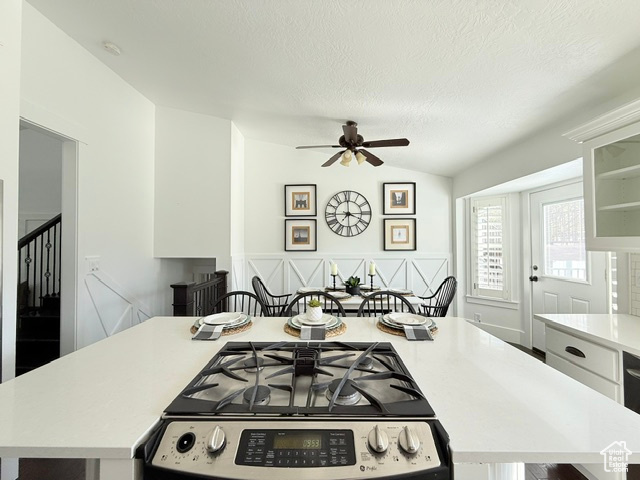 Kitchen with stainless steel gas range, light countertops, a textured ceiling, a ceiling fan, and vaulted ceiling