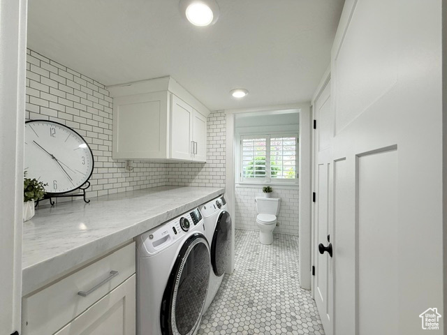 Laundry room with washer and dryer, light tile patterned floors, cabinet space, and tile walls