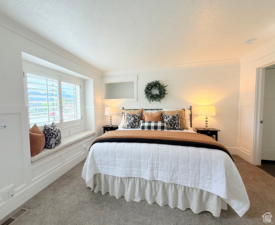 Bedroom with a textured ceiling, a decorative wall, visible vents, and carpet floors