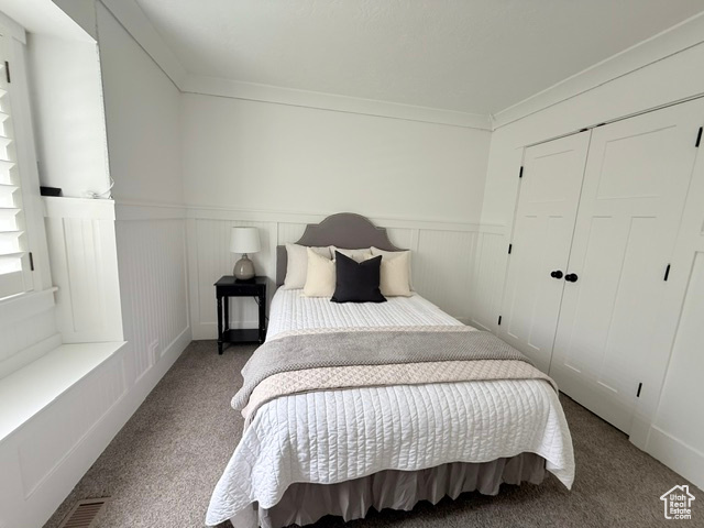 Carpeted bedroom featuring a wainscoted wall, a closet, and crown molding