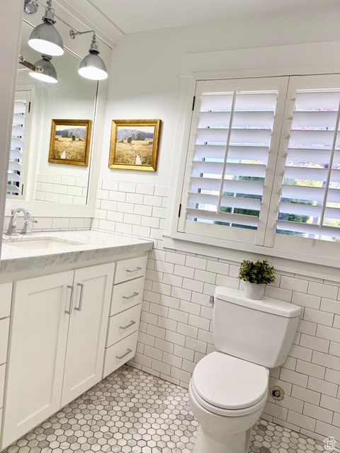 Half bath with toilet, tile patterned floors, tile walls, and vanity