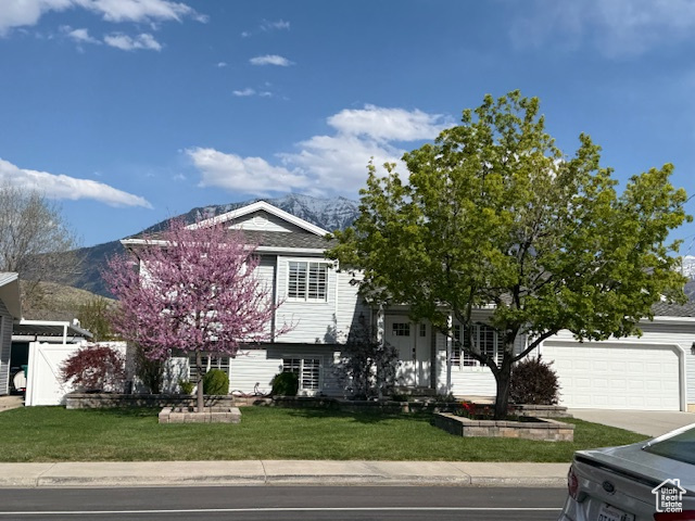 View of front of property with concrete driveway, an attached garage, a mountain view, and a front yard