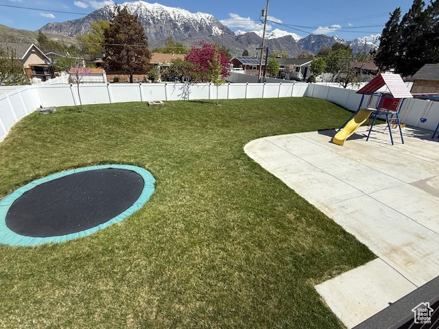 View of yard featuring a playground, a mountain view, a fenced backyard, and a trampoline