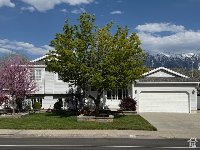 View of front of house featuring a garage, a front lawn, a mountain view, and driveway