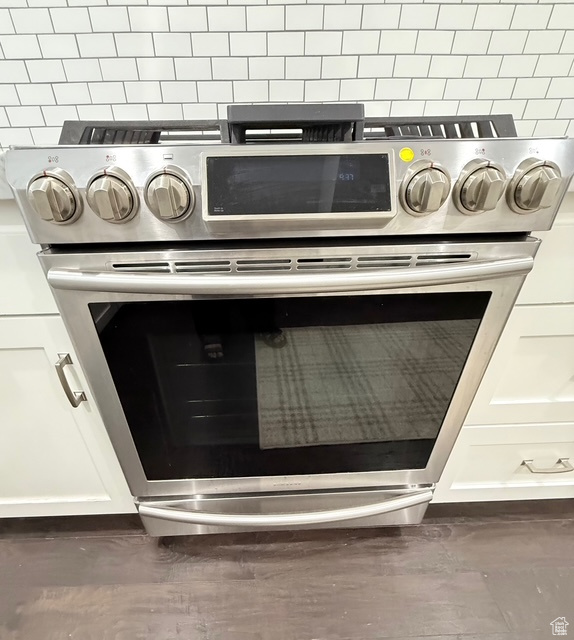Room details with stainless steel range with gas stovetop, backsplash, white cabinetry, and wood finished floors