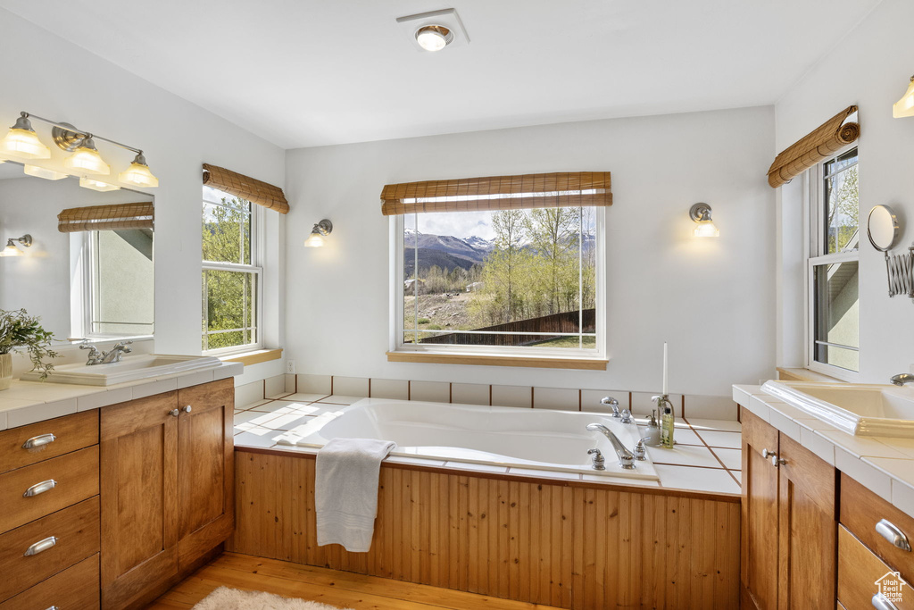 Full bath featuring vanity, a garden tub, and wood finished floors
