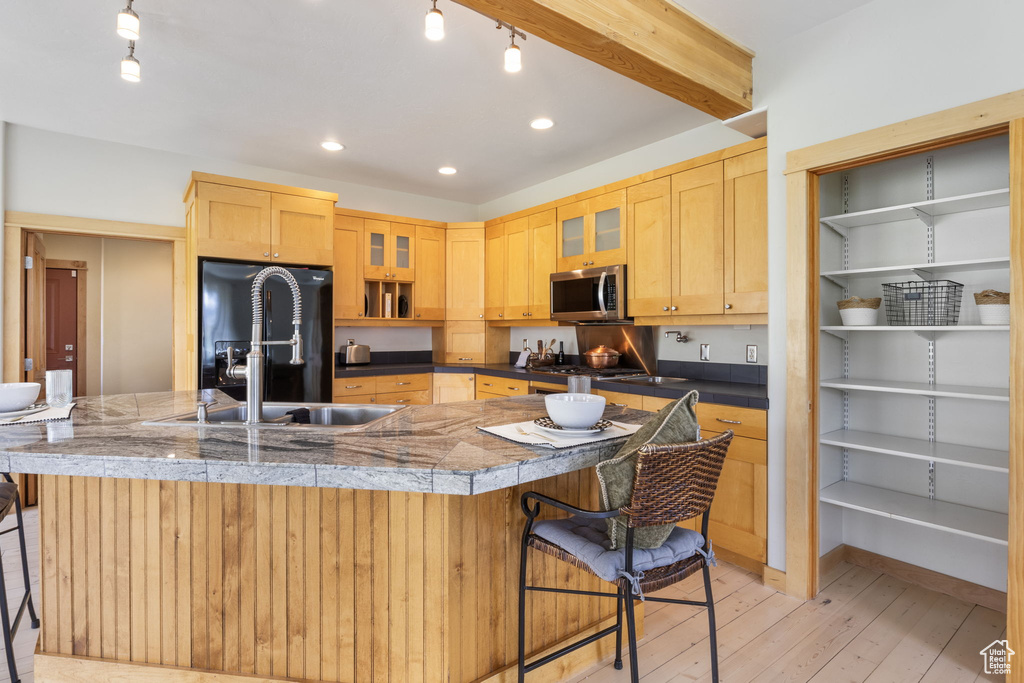 Kitchen featuring stainless steel microwave, a breakfast bar, light wood-type flooring, and black fridge