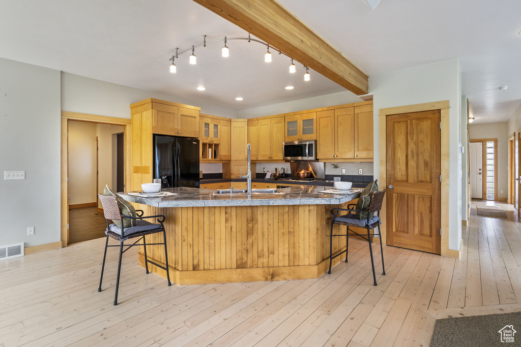Kitchen featuring a kitchen breakfast bar, stainless steel microwave, visible vents, glass insert cabinets, and black fridge with ice dispenser