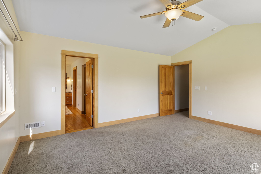 Unfurnished bedroom featuring visible vents, baseboards, ensuite bathroom, light colored carpet, and vaulted ceiling