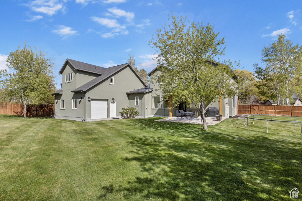 Rear view of property with a trampoline, stucco siding, a yard, and fence