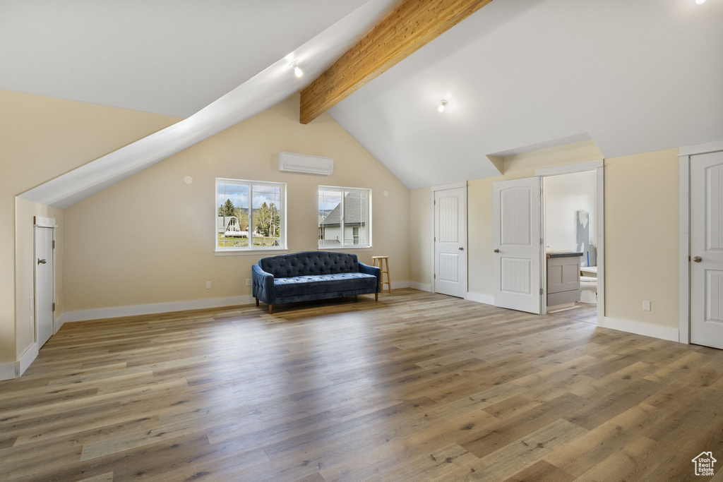 Interior space with vaulted ceiling with beams, baseboards, light wood-style flooring, and a wall mounted AC