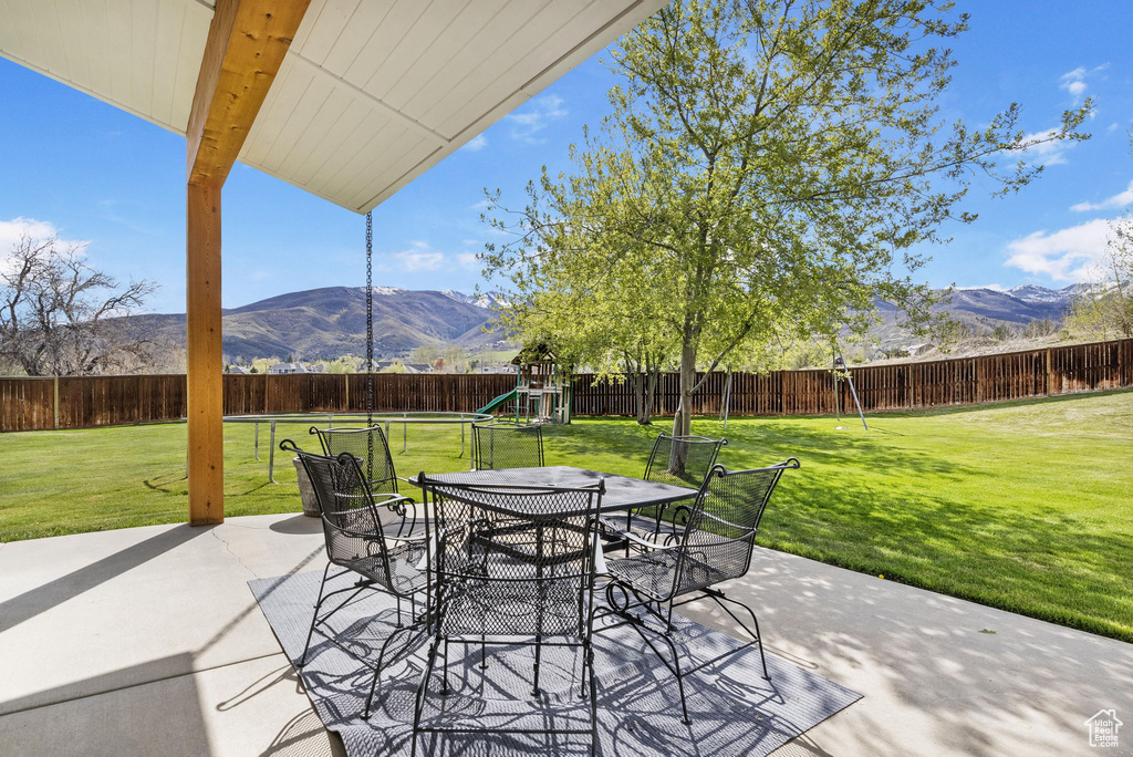 View of patio / terrace with a playground, a mountain view, a fenced backyard, and outdoor dining space