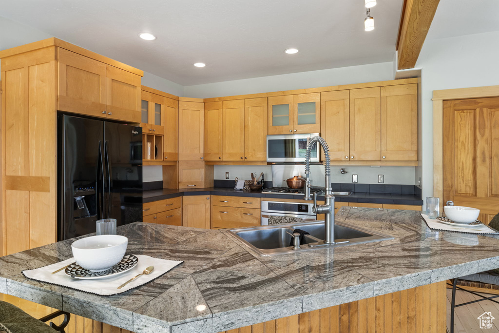 Kitchen with black fridge with ice dispenser, glass insert cabinets, a kitchen bar, stainless steel microwave, and a sink
