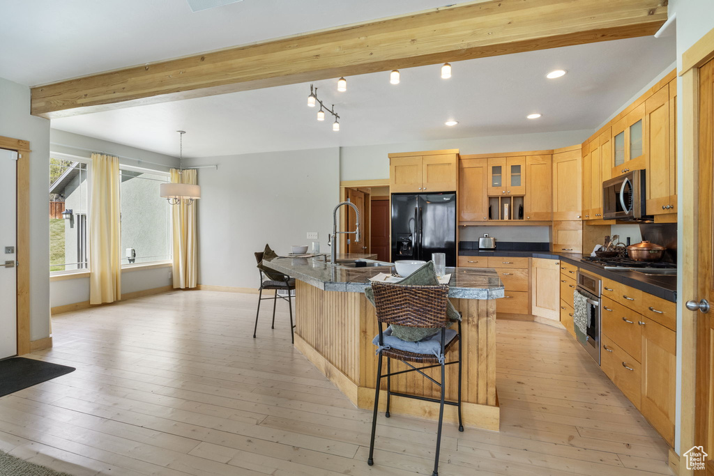 Kitchen with dark countertops, beam ceiling, a sink, a breakfast bar, and stainless steel appliances