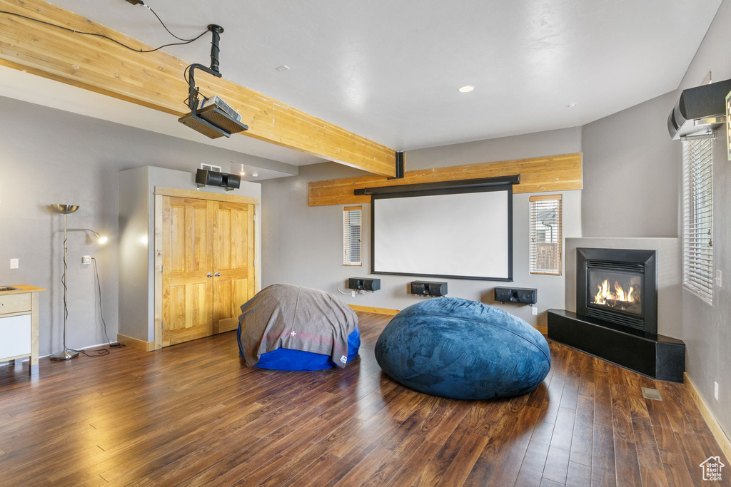 Home theater with beam ceiling, wood-type flooring, a glass covered fireplace, recessed lighting, and baseboards