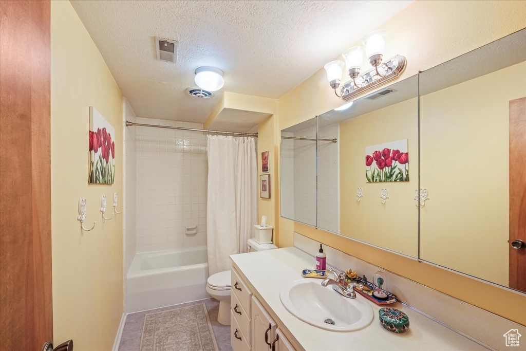 Bathroom featuring vanity, tile patterned flooring, shower / bath combo with shower curtain, toilet, and a textured ceiling
