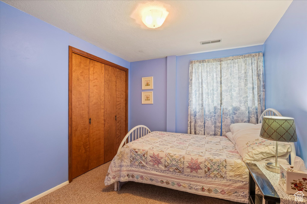 Bedroom with carpet flooring, visible vents, and a closet