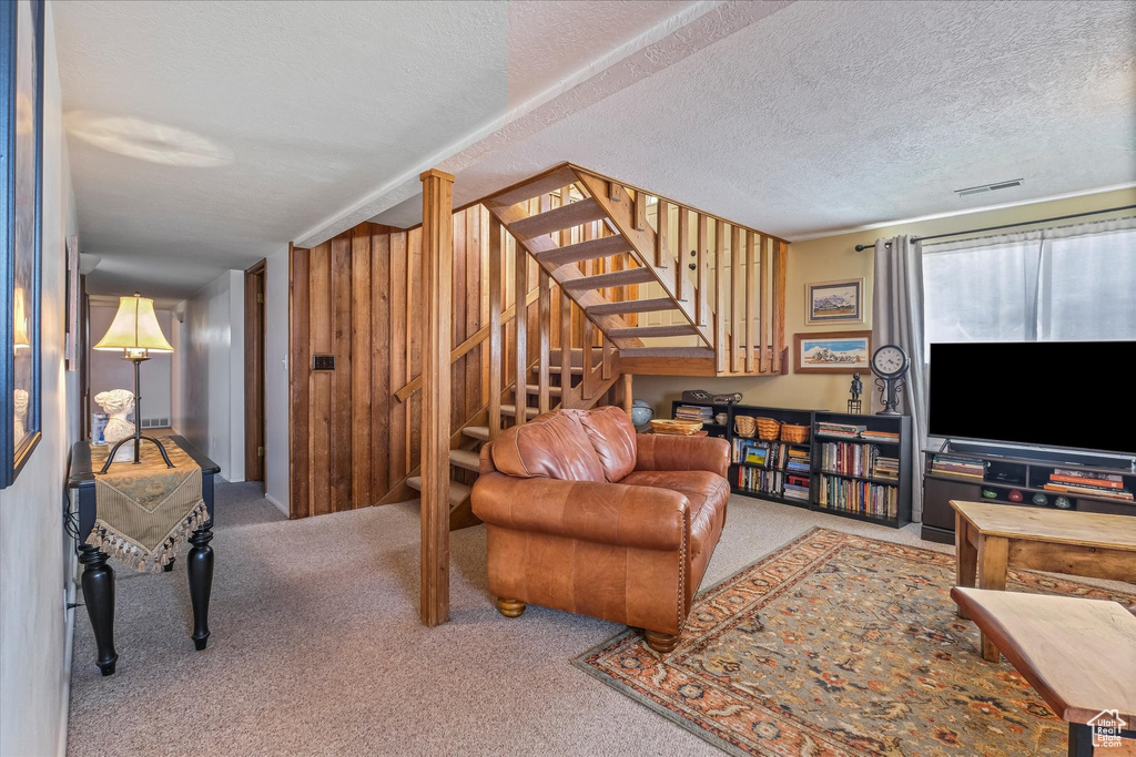 Living area with a textured ceiling, wood walls, carpet, visible vents, and stairway