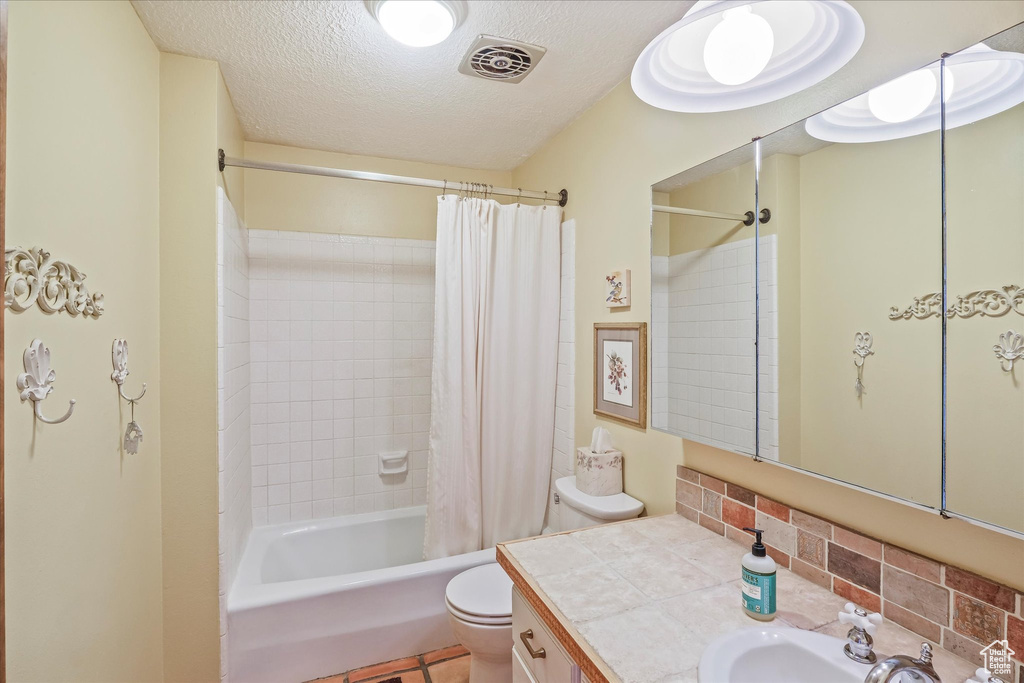 Full bathroom featuring shower / tub combo with curtain, vanity, toilet, a textured ceiling, and visible vents