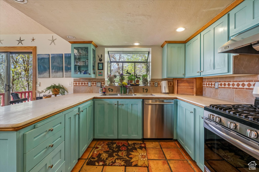 Kitchen featuring appliances with stainless steel finishes, light countertops, a textured ceiling, a peninsula, and backsplash