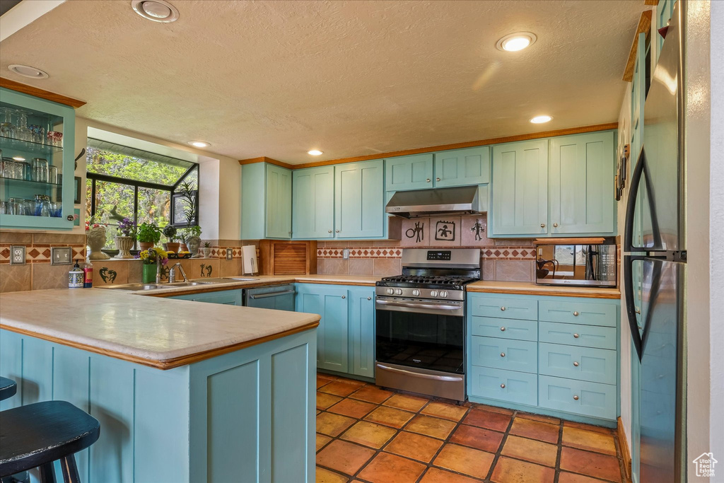 Kitchen featuring a textured ceiling, stainless steel appliances, backsplash, a peninsula, and under cabinet range hood