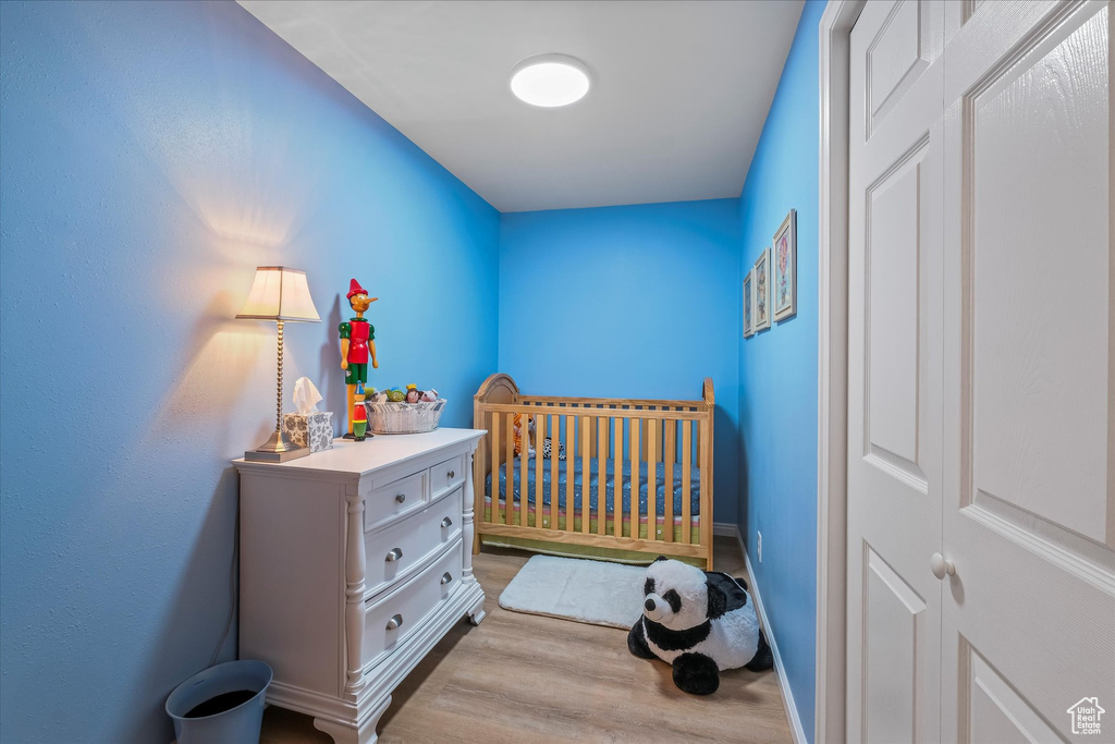 Bedroom featuring a nursery area, baseboards, and wood finished floors