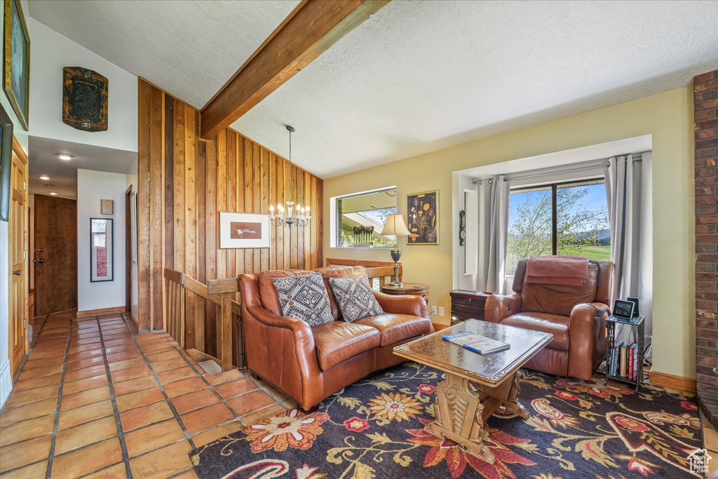 Living room featuring a textured ceiling, wood walls, tile patterned floors, a chandelier, and vaulted ceiling with beams