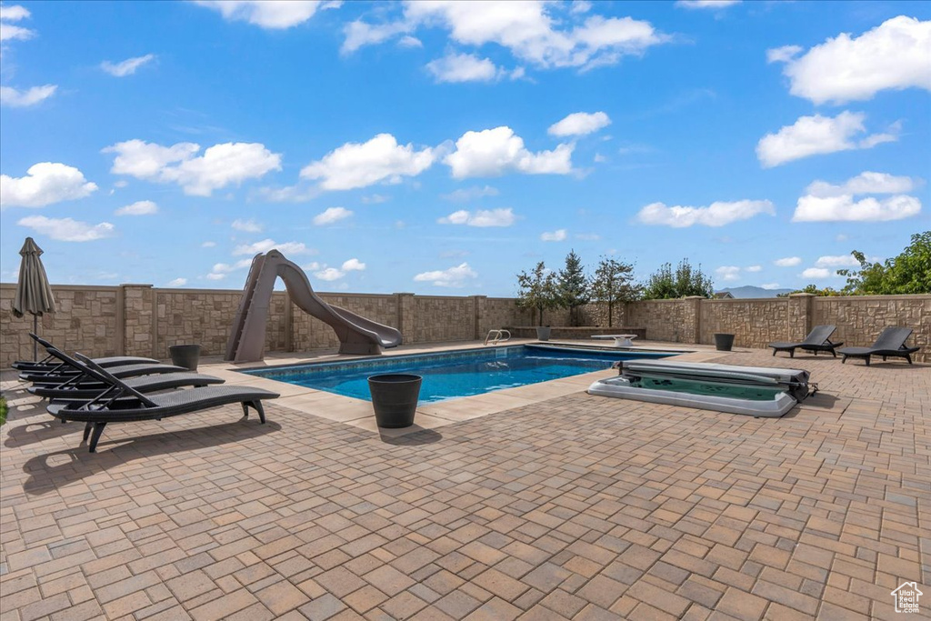 View of swimming pool with a diving board, a fenced in pool, a fenced backyard, a patio, and a water slide