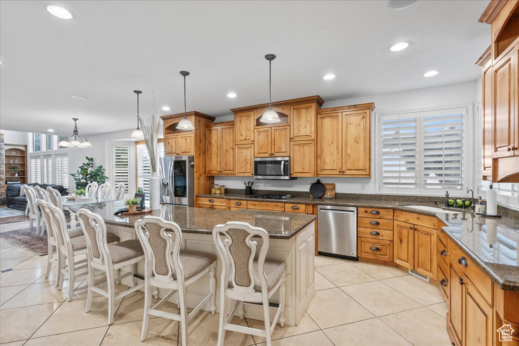 Kitchen with appliances with stainless steel finishes, a center island, a chandelier, dark stone counters, and light tile patterned flooring