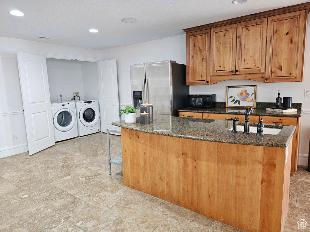 Kitchen with brown cabinetry, washing machine and clothes dryer, black microwave, a sink, and stainless steel fridge