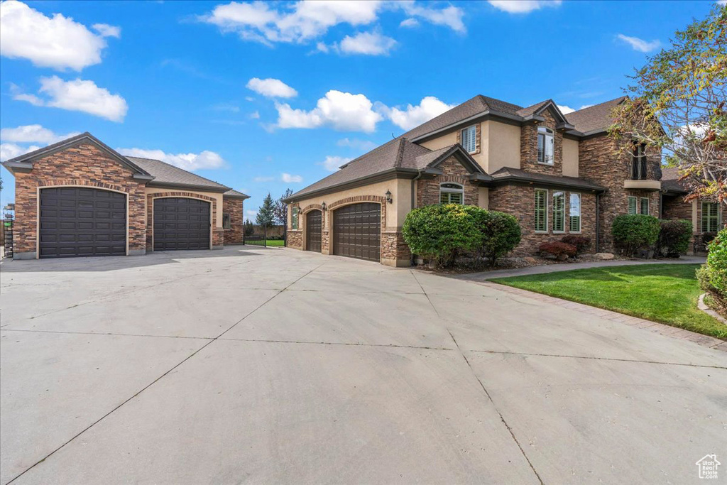 View of front of property with driveway, a front yard, an attached garage, stone siding, and stucco siding