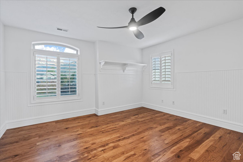 Empty room with visible vents, wainscoting, ceiling fan, and wood finished floors