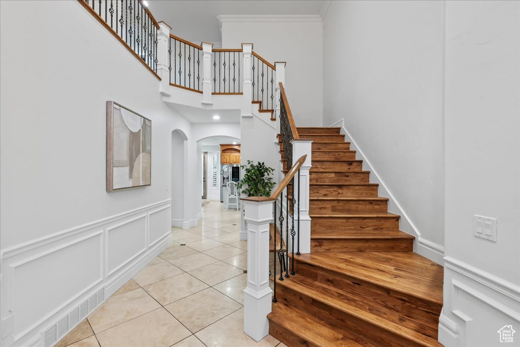 Stairs featuring a towering ceiling, crown molding, arched walkways, baseboards, and tile patterned floors