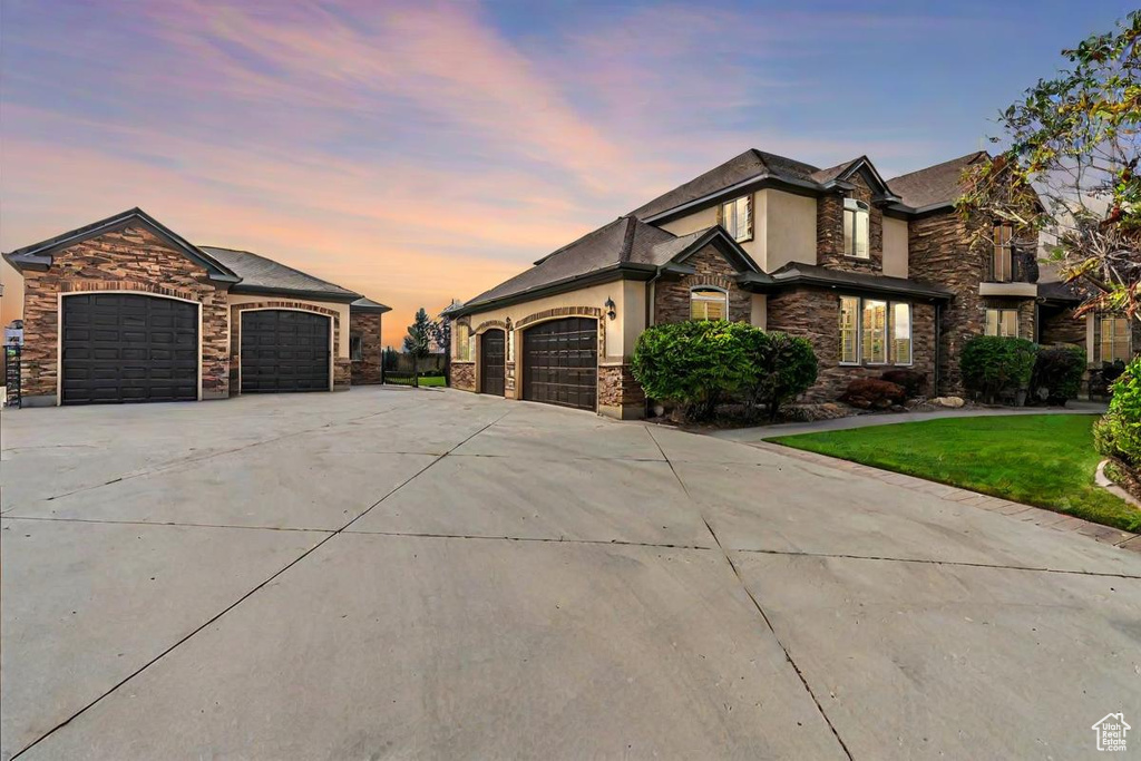 View of front of home featuring stone siding, a garage, stucco siding, a lawn, and driveway