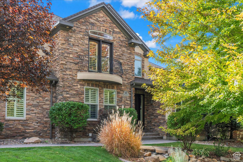 View of front of home with a front yard, a balcony, and stone siding