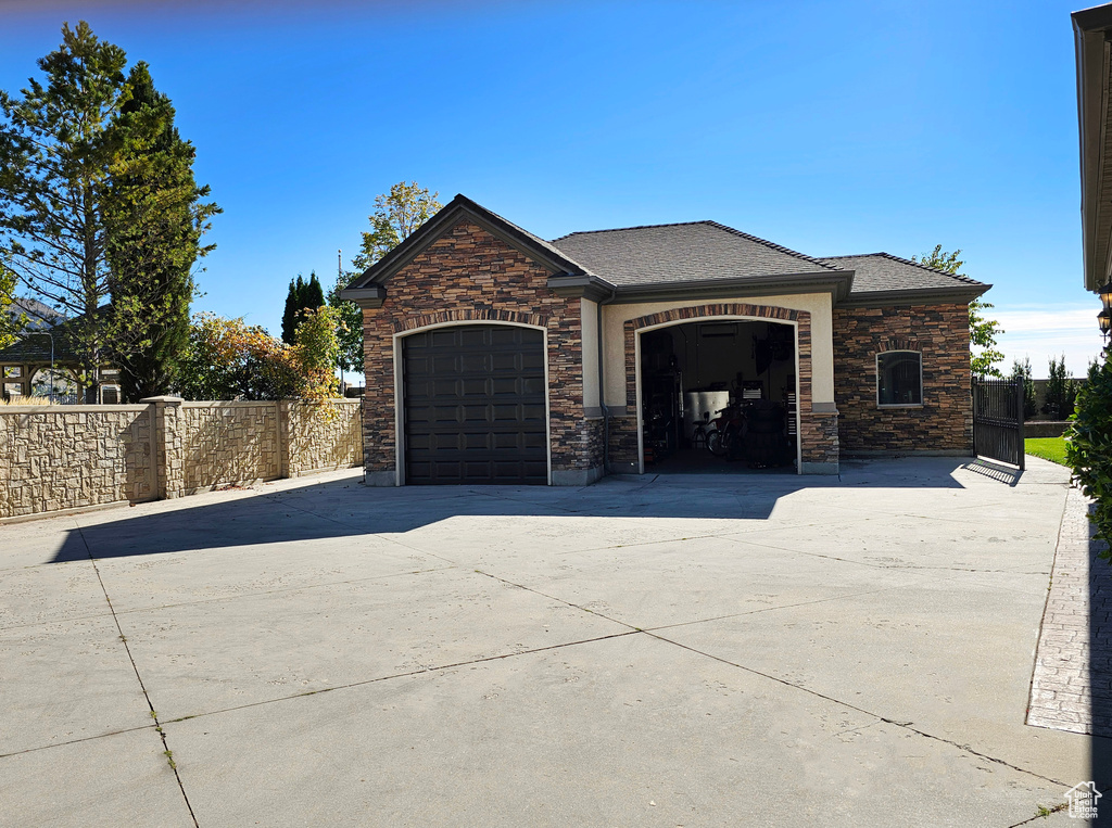 View of front of house with a garage, fence, driveway, and stone siding